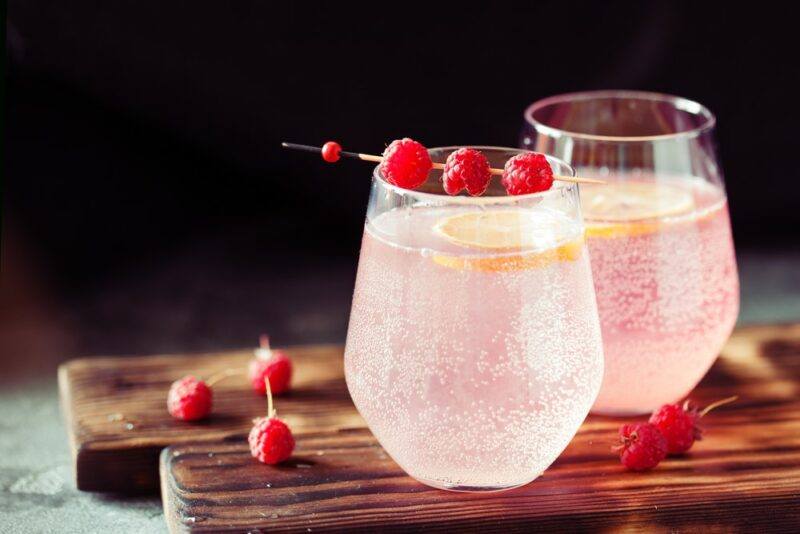 Two glasses containing a sparkling pink White Claw martini with a lemon slice, one of which is garnished with three raspberries on a stick