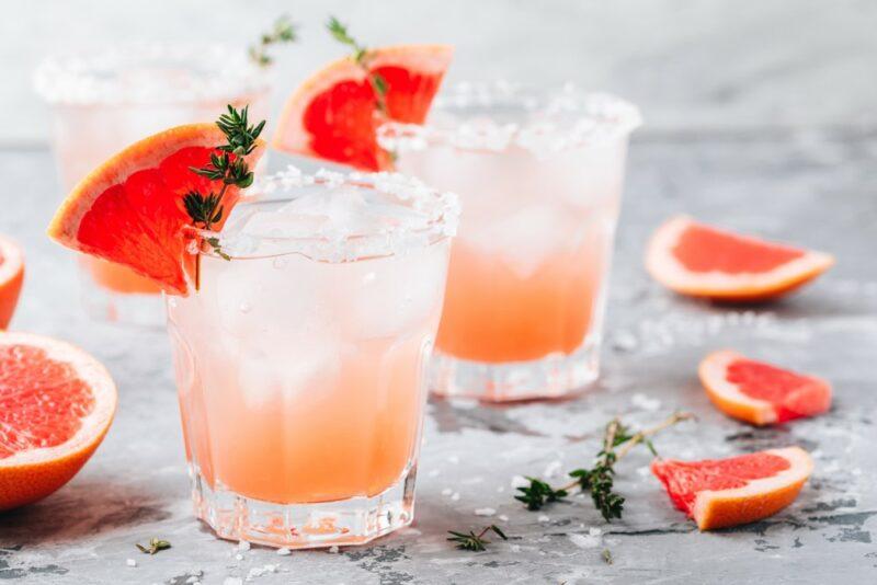 Two glasses containing a moonlight paloma cocktail surrounded by slices of grapefruit