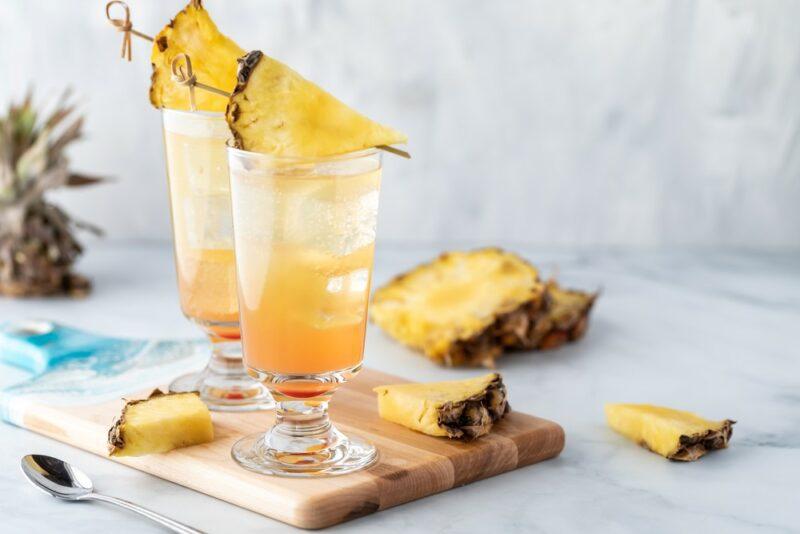 Two tall glasses containing a pineapple coconut mimosa with wedges of pineapple as the garnish