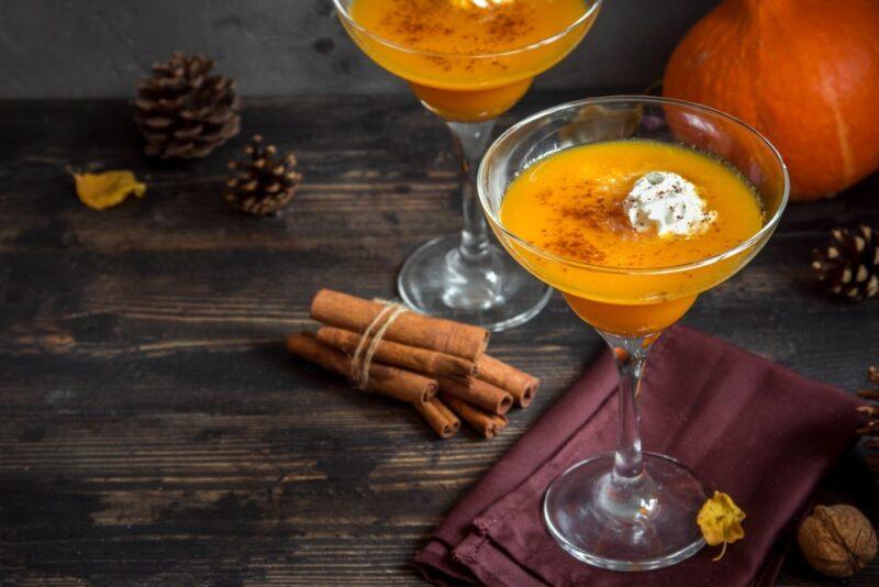 Margarita glasses containing a pumpkin pie punch cocktail on a wooden table with sticks of cinnamon