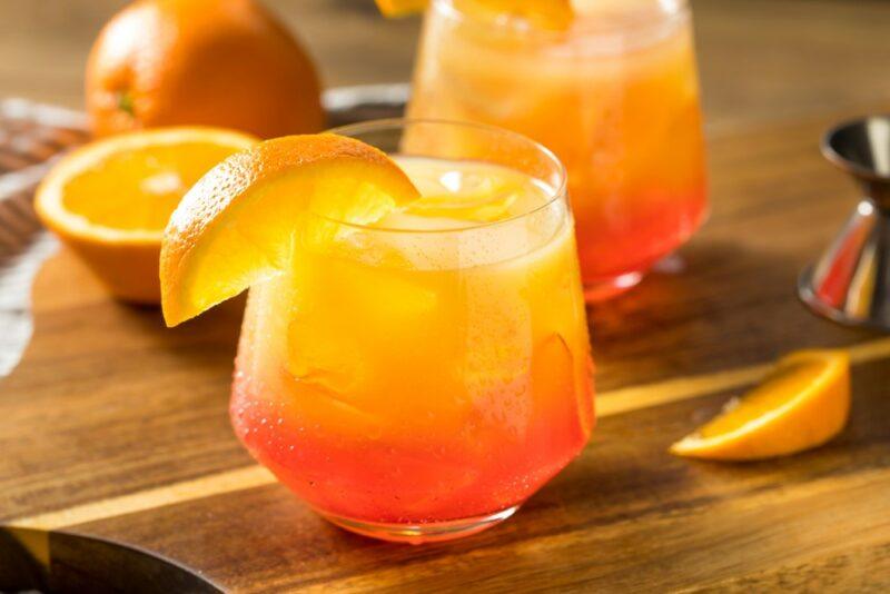 A wooden board with two glasses of a tequila sunrise cocktail and oranges