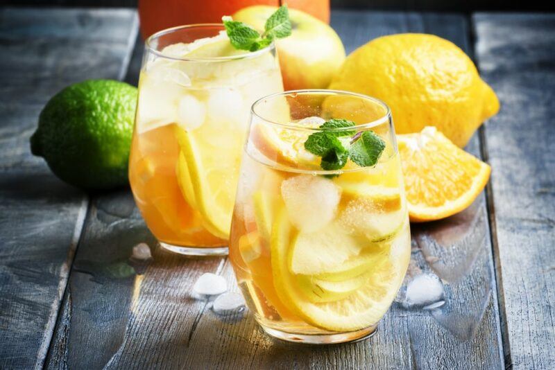 Two glasses of a white sangria cocktail with plenty of fresh fruit inside and more behind