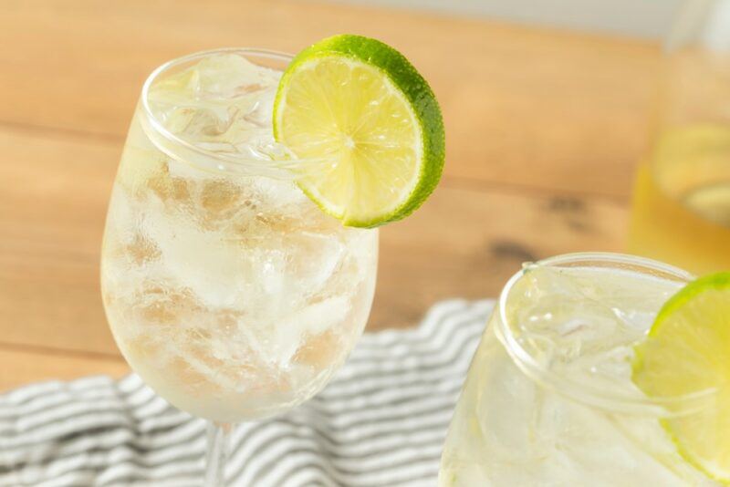 A wooden table with a lined cloth and two wine glasses containing a white wine spritzer garnished with a slice of lime