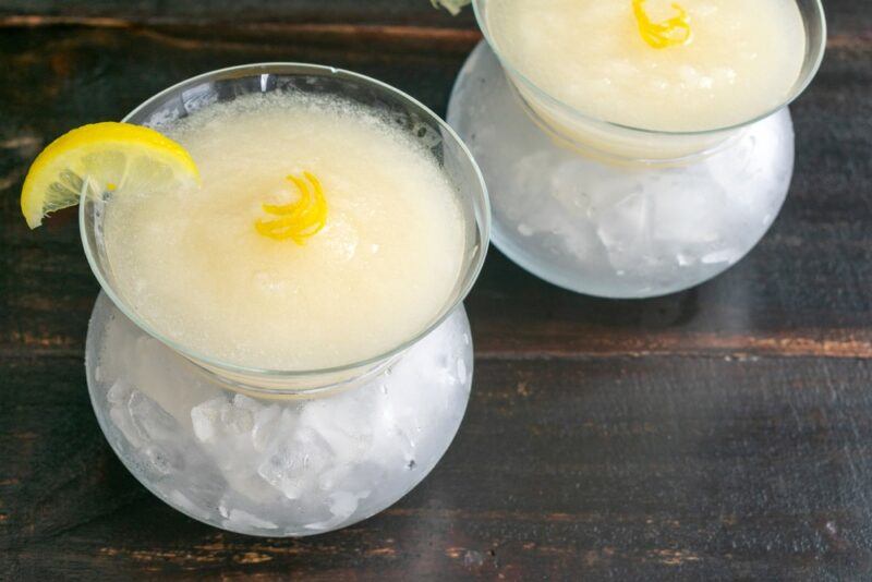 Two martini glasses containing a frozen prosecco cocktail, each garnished with a piece of lemon