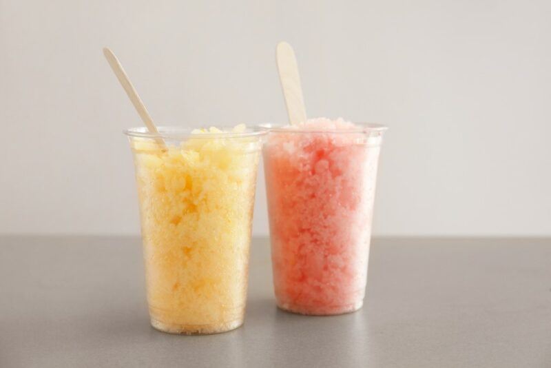 A table with two glasses of snow cone, one raspberry one peach, highlighting the idea of peach razzmatazz