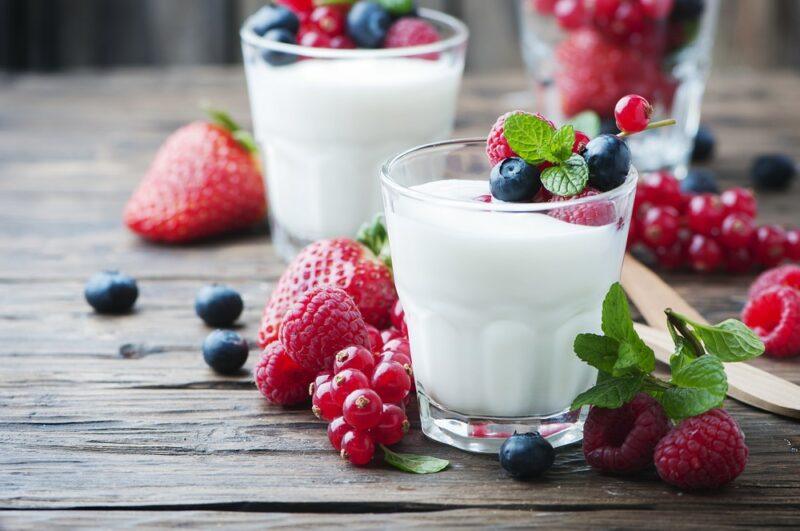 A brown wooden table with two glasses of yogurt and berries, plus more berries on the table