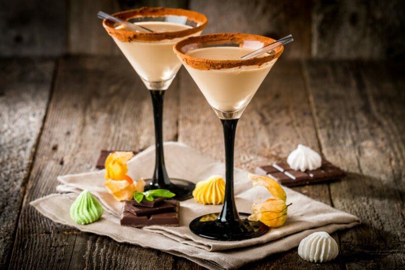 Two cocktail glasses containing Baileys Apple Pie Liqueur with some treats or candies on the table around the base of the glasses