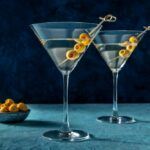 Two Churchill martinis with olives as a garnish, next to a small bowl of olives