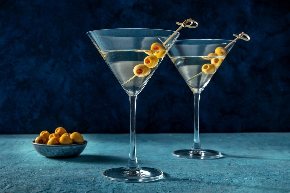 Two Churchill martinis with olives as a garnish, next to a small bowl of olives