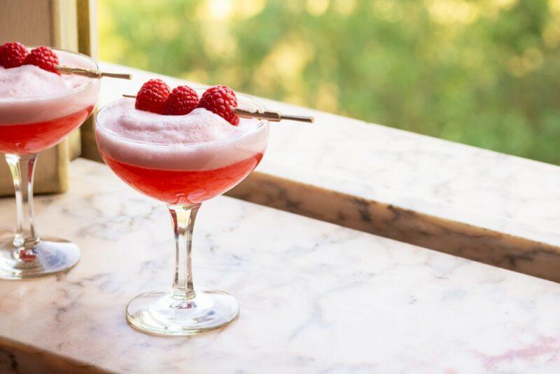 Two glasses of a Clover Club cocktail with plenty of froth, garnished with three raspberries