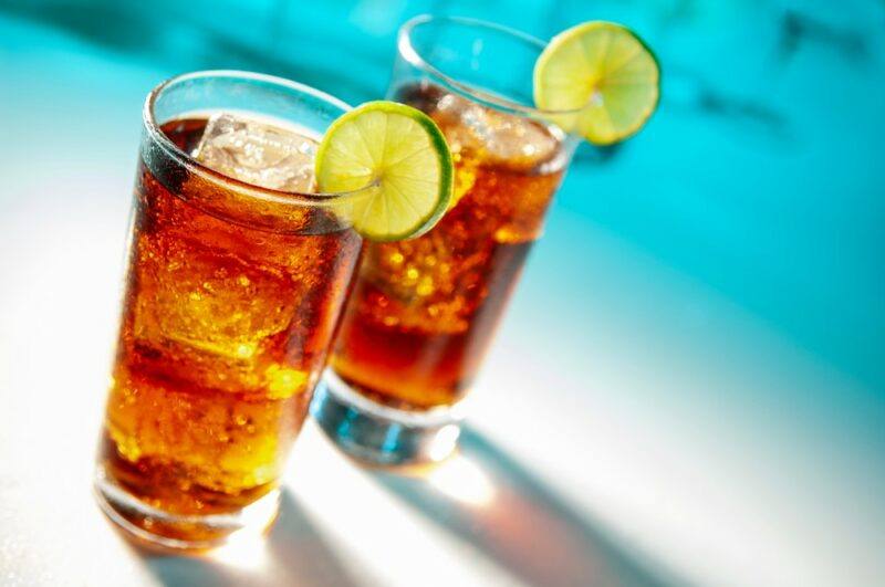 Two glasses containing a Lynchburg beer cocktail with slices of lime as a garnish, in front of the ocean