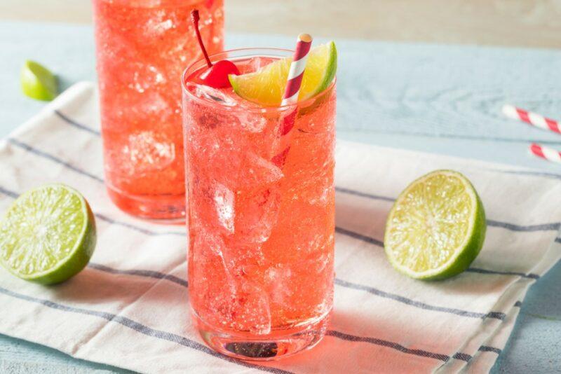 Two highball glasses containing a White Claw black cherry limeade cocktail with a straw, next to some lime halves