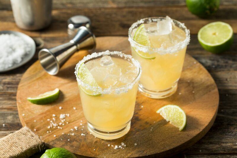 A wooden board with two White Claw margarita spritzer cocktails, salt, lime wedges, and a cocktail jigger