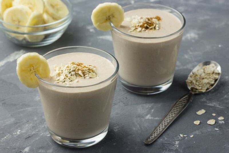 Two glasses of a banana smoothie with bananas, next to a glass bowl of bananas