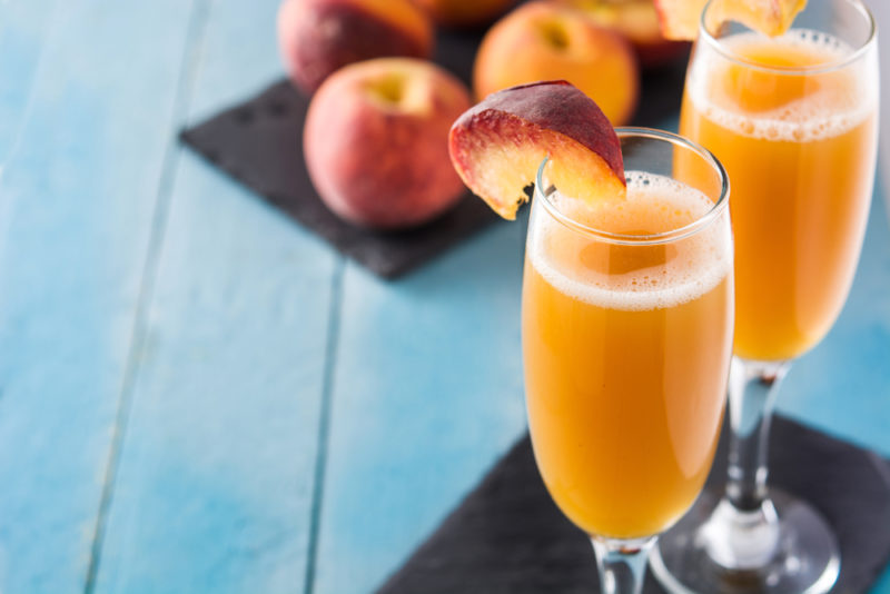 Two glasses of bellini on a black cloth and some peaches on a black cloth in the background