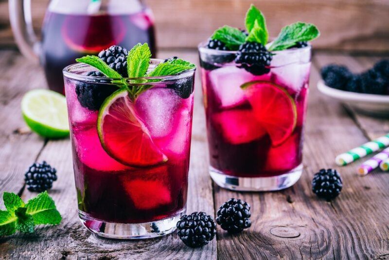 Two glasses of a tequila blackberry smash, which includes ice, mint leaves, citrus slices, and blackberries