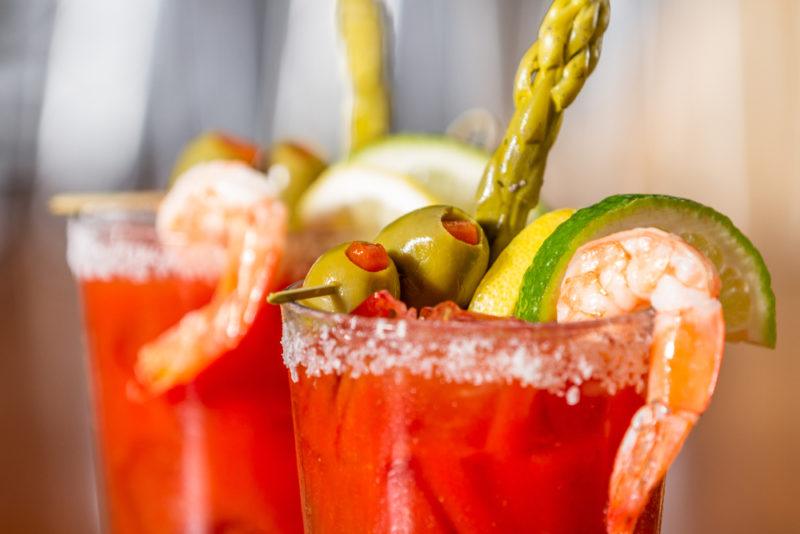 Two bloody Mary cocktails with a selection of garnishes, including shrimp and asparagus