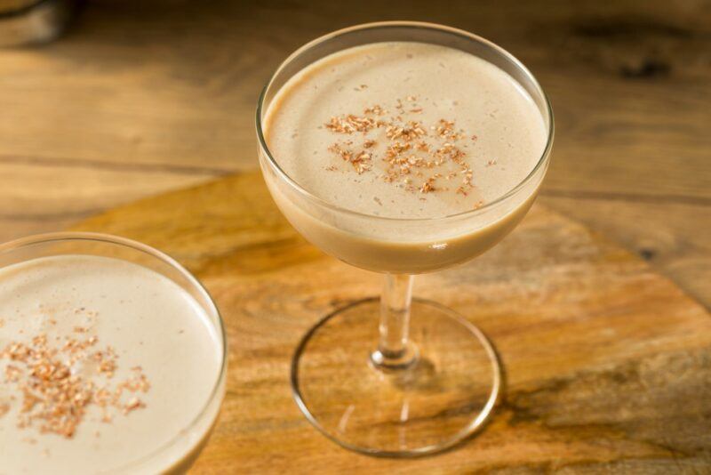 A wooden table with two coupe glasses containing a chocolate and peanut butter cocktail