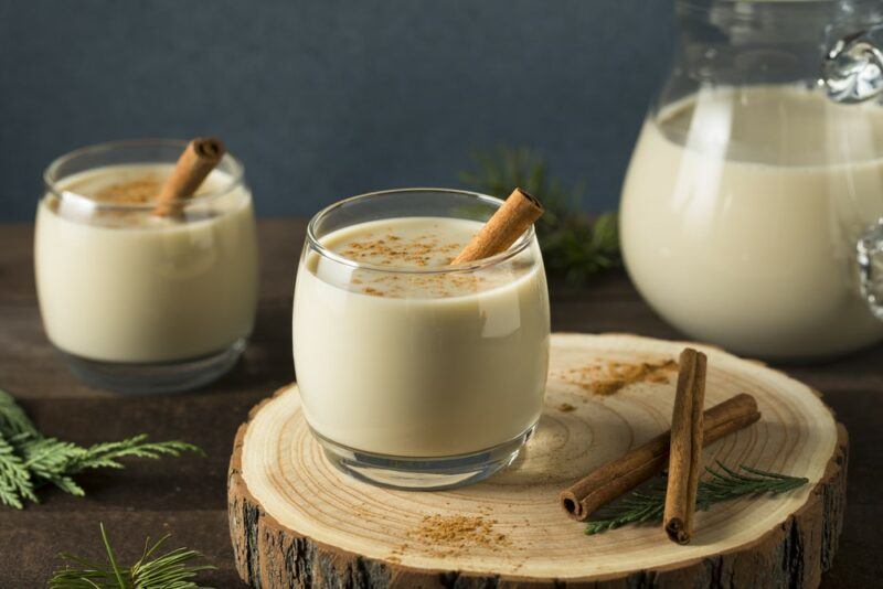 Two glasses of an eggnog like cocktail made using vanilla rum, with a jug of the cocktail in the background