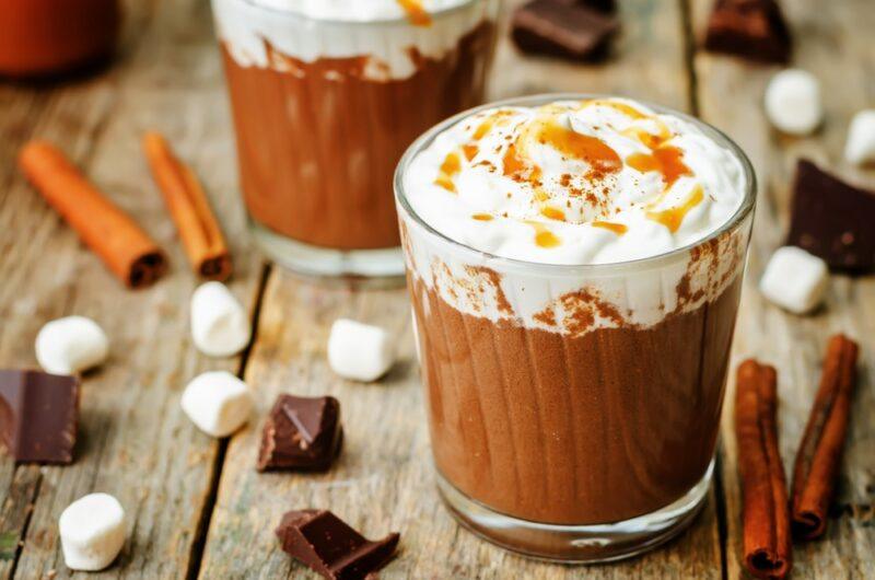 Two large glasses of caramel hot chocolate with cream and caramel on the top, which includes rum