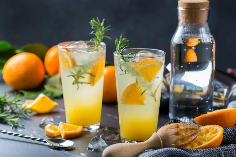 Two glasses containing a gin St. Clements cocktail, each with orange pieces, gin, and a sprig of rosemary