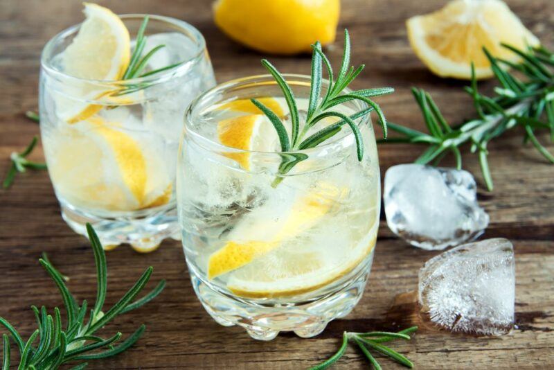 A wooden table with a glass containing ice, lemon, and rosemary