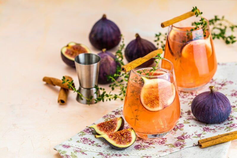 Two glasses containing a honey cosmopolitan cocktail with plenty of figs in the cocktail and on the table