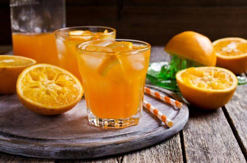 A circular wooden tray with straws, orange halves, and glasses containing a morning mule cocktail