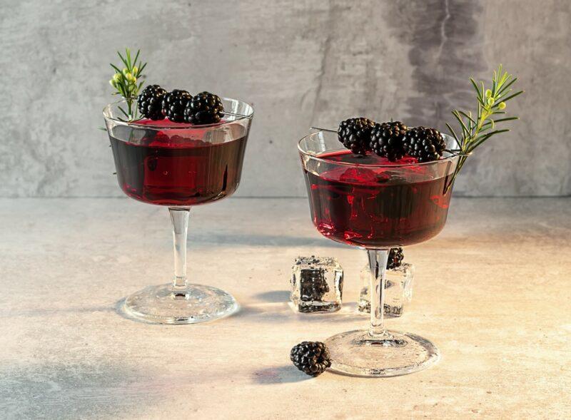 Two glasses containing a peanut butter thyme cocktail, each garnished with three blackberries and a sprig of thyme