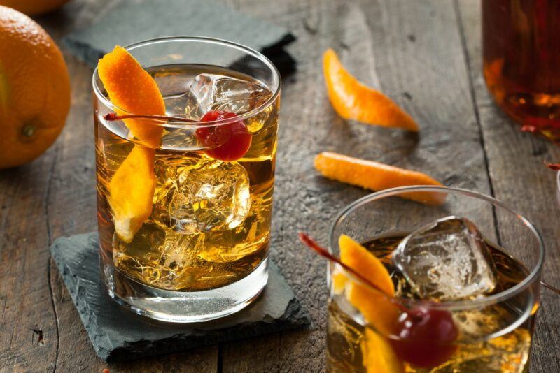 Two glasses containing a peanut butter whiskey old fashioned cocktail with orange twists