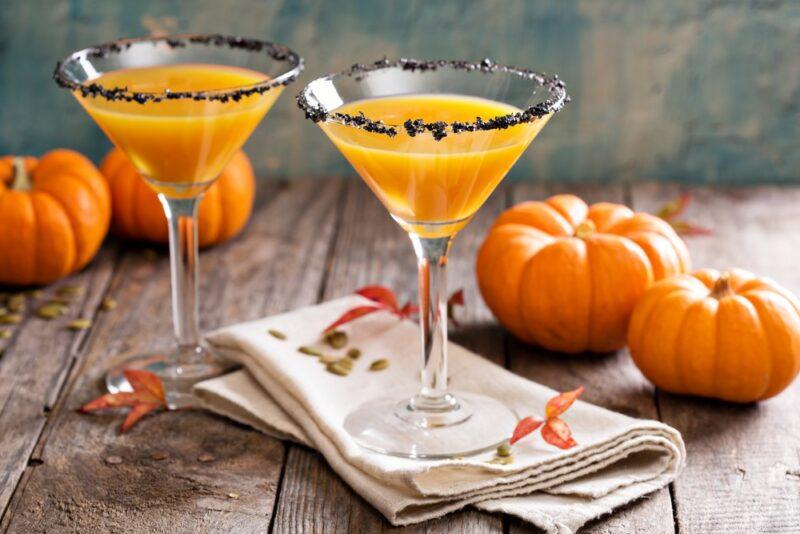 Two martini glasses containing a pumpkin pie martini with various pumpkins on the table