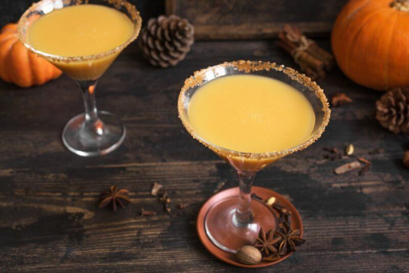 Two pumpkintini cocktails with sugar rims on a wooden table next to pinecones