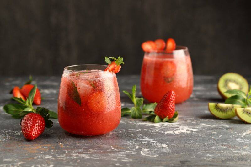 Two glasses containing a strawberry sex on the beach cocktail, next to some strawberries and kiwis