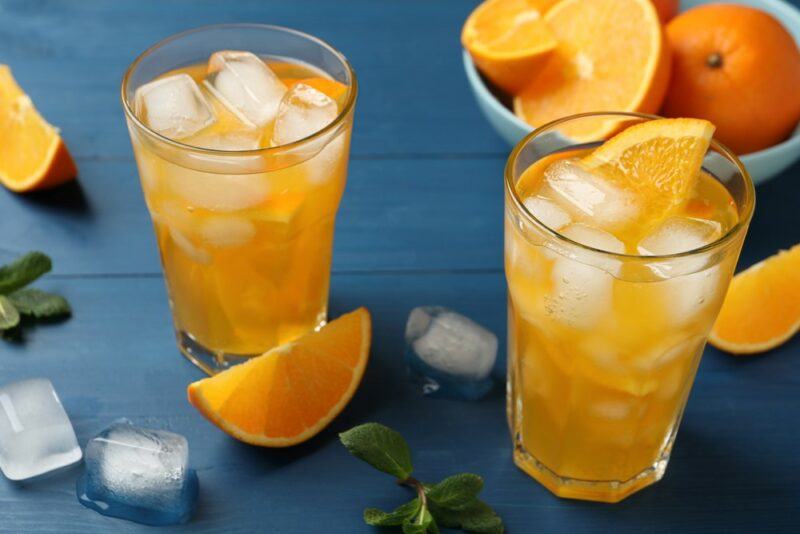 Two glasses of a sunflower highball cocktail with ice next to a bowl of oranges