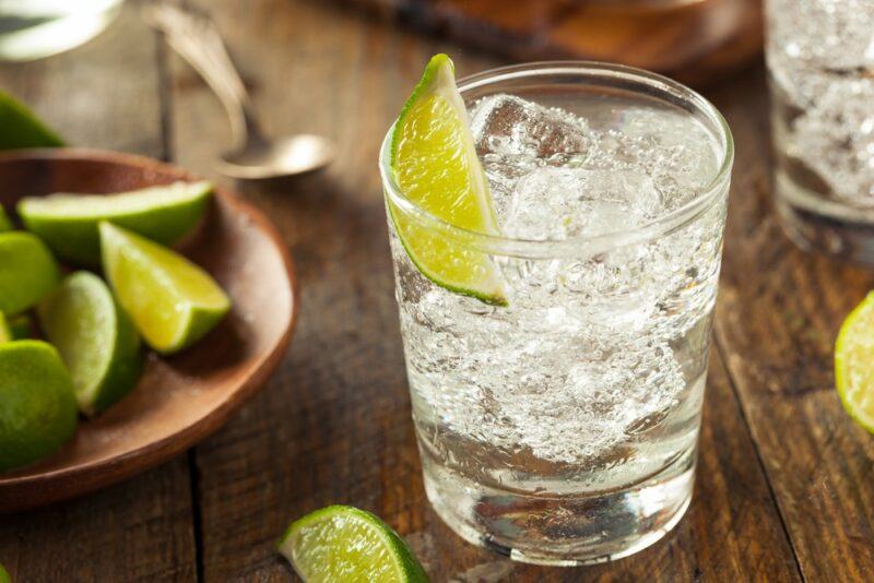 A single glass of vodka tonic made with plenty of ice and a lime wedge. There's a plate of lime wedges on the table next to the glass.