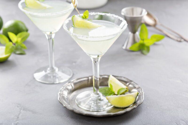 A glass of a white wedding cocktail on a metal tray, next to another one on a table