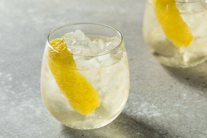 Two stemless wine glasses on a gray table containing a wine cooler, ice, and lemon zest