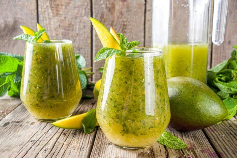 Two glasses of aam panha, next to a jug of the drink - on a wooden table, in front of a wooden wall