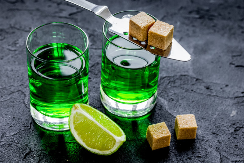 Two glasses of green absinthe with cubes of brown sugar and a wedge of lime