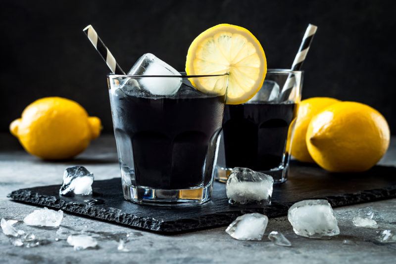 Two cocktails made with squid ink with straws, ice, and lemons