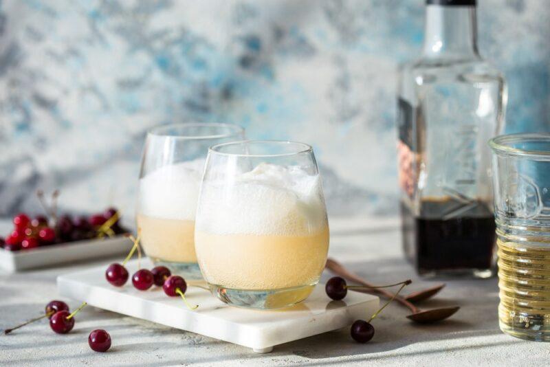 A bottle of alcohol next to two glasses of an orange creamsicle cocktail