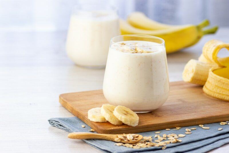 Two glasses of a banana smoothie, with fresh bananas in the background