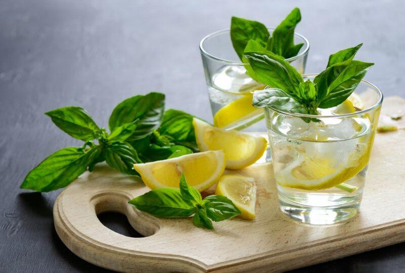 Two glasses of basilcello liqueur on a wooden board with plenty of basil and lemon