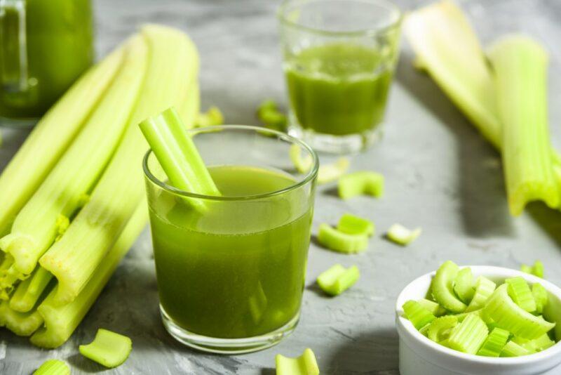 Two glasses containing celery juice with sticks of celery poking out, along with many pieces of celery