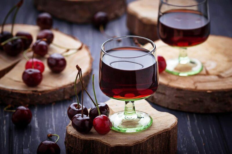 Two glasses of cherry pie moonshine or a similar drink on slabs with some fresh cherries