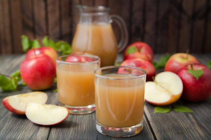 Two glasses and a jug of cloudy apple juice, surrounded by apples