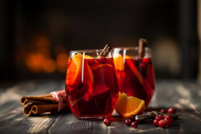 Two glasses filled with cranberry mulled wine on a wooden table with cinnamon sticks and fruit on the table