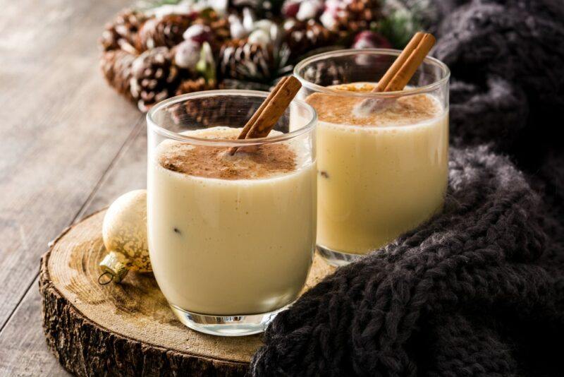 A wooden board with two glasses of eggnog with cinnamon sticks as a garnish