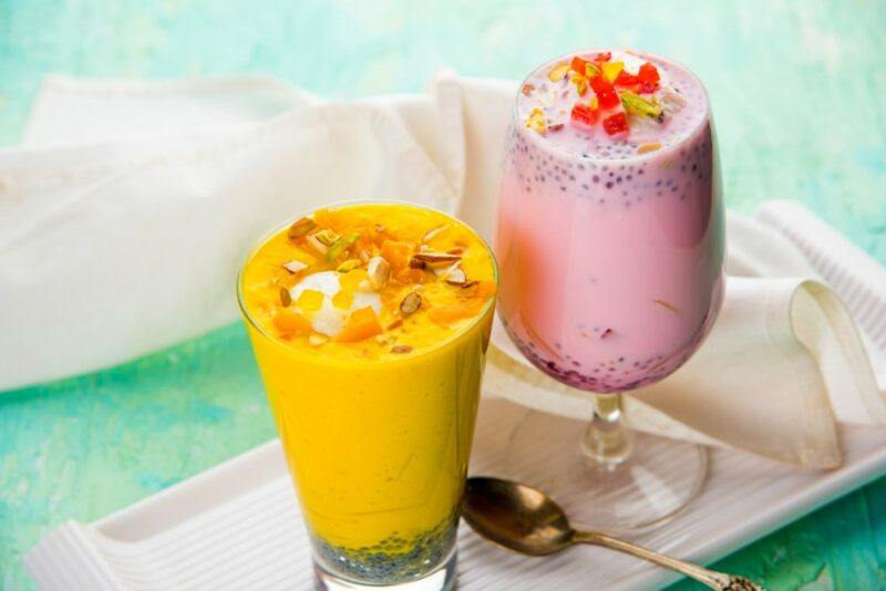 A glass of pink falooda and one of yellow falooda on a white dish and a green table