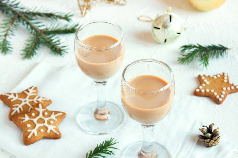 Two glasses of gingerbread liqueur on a white table with gingerbread cookies and pine fronds